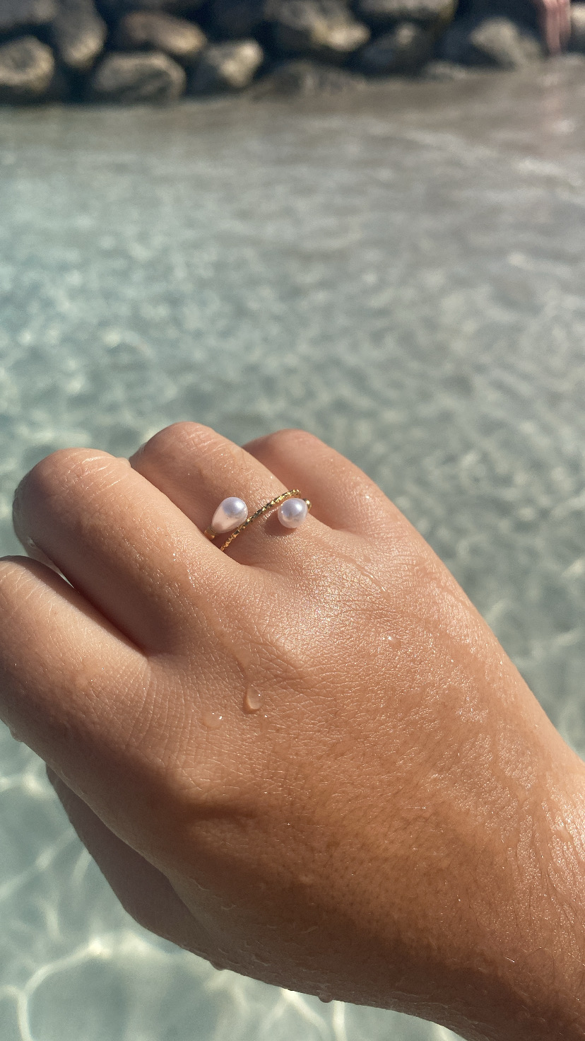 Anel dourado com pérolas em mão sobre água clara