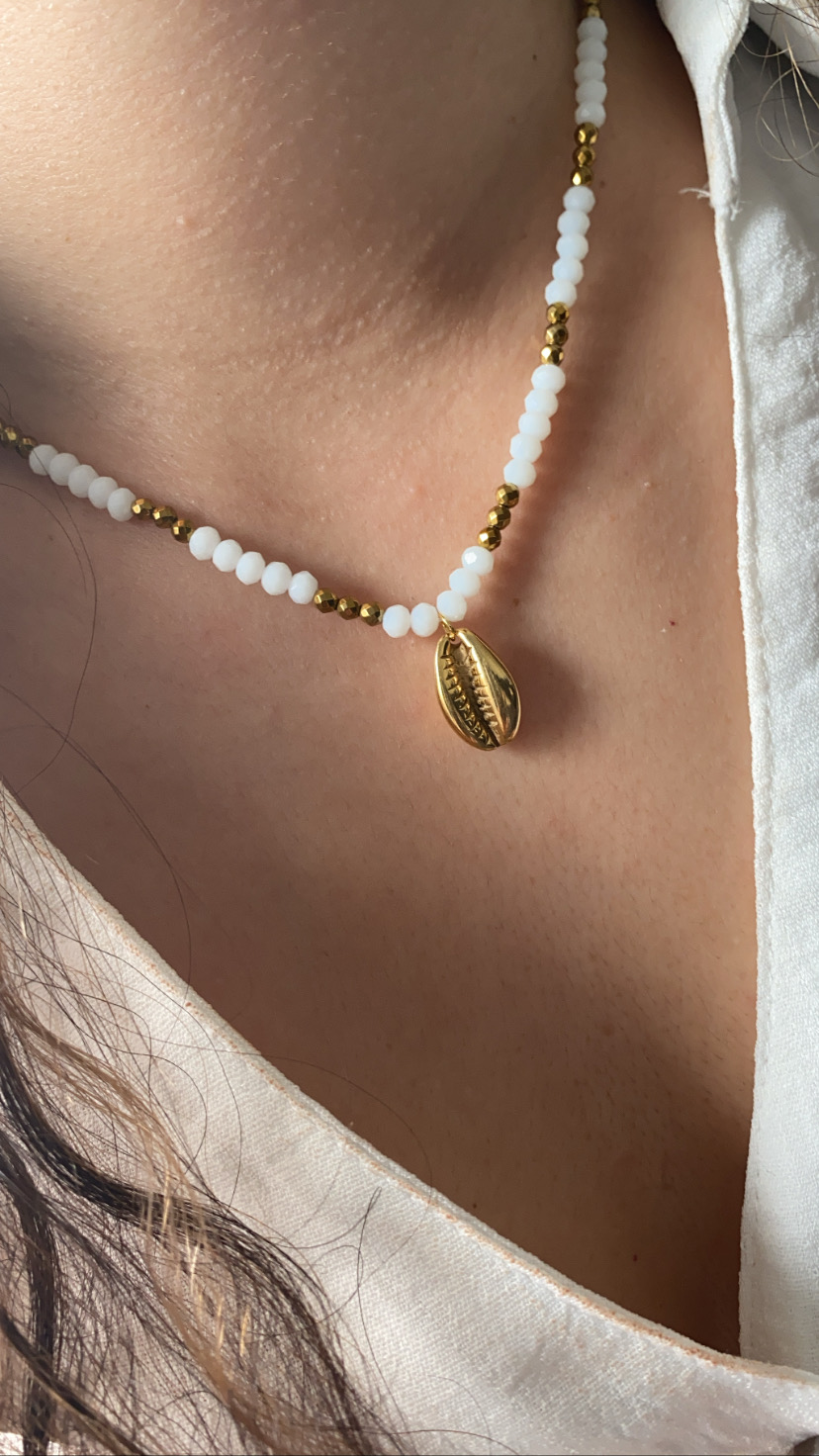 Colar com contas brancas e douradas com pendente de concha dourada no pescoço