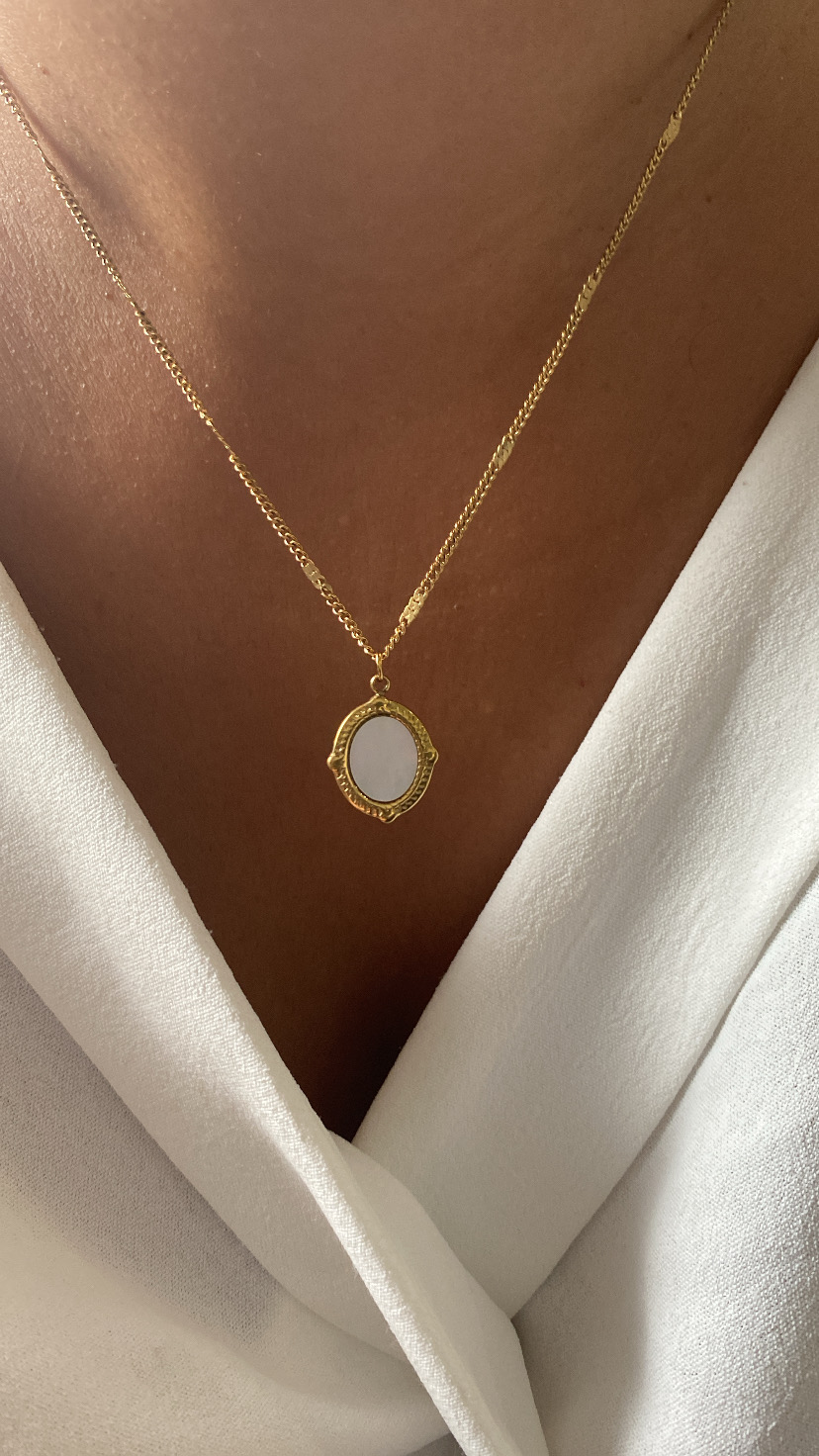 Colar dourado com pendente oval branco em pele morena e camisa branca