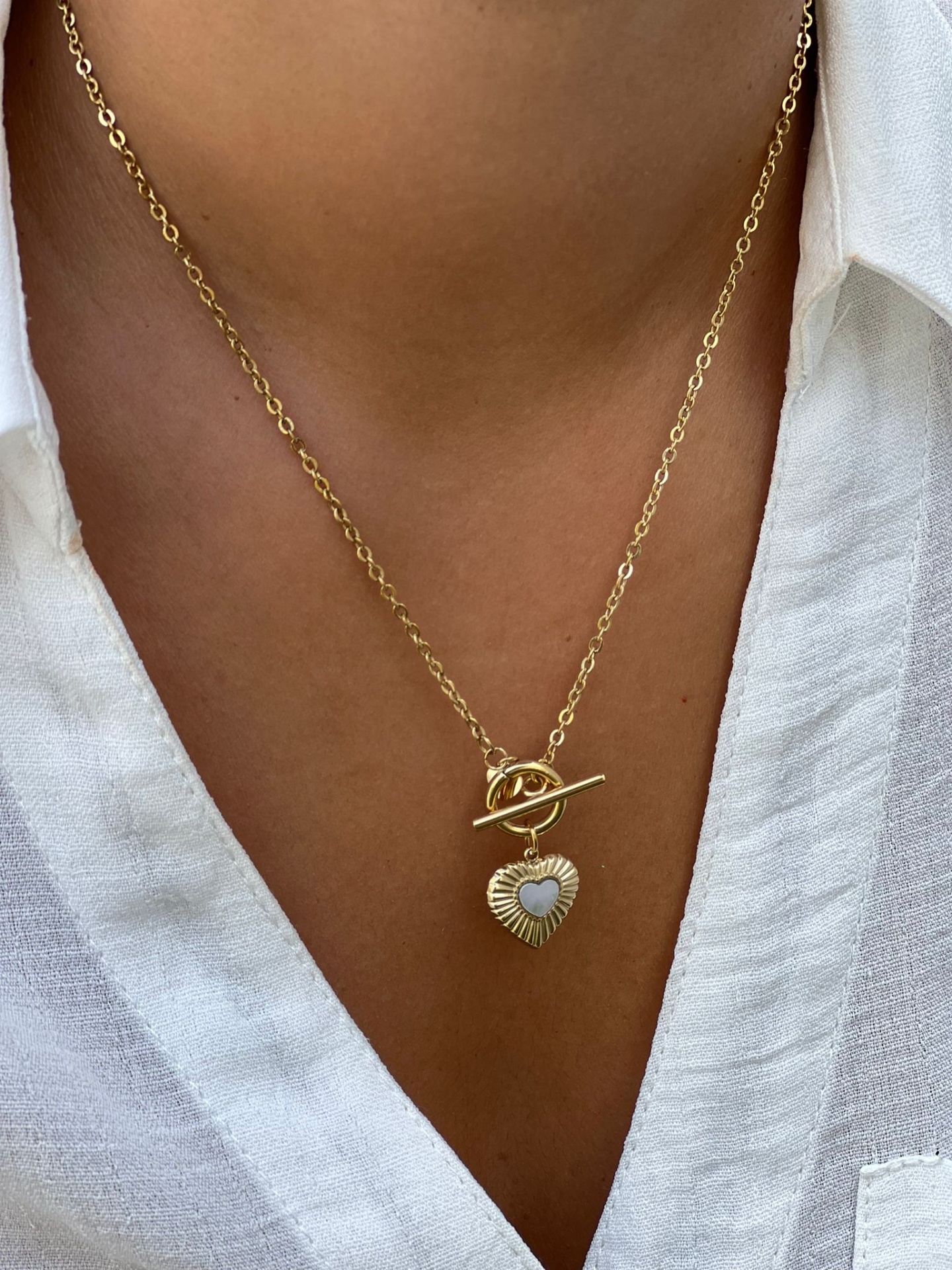Colar dourado com pendente de coração, usado com camisa branca