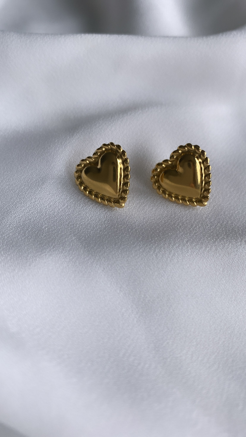 Brincos coração dourados com borda texturizada sobre tecido branco