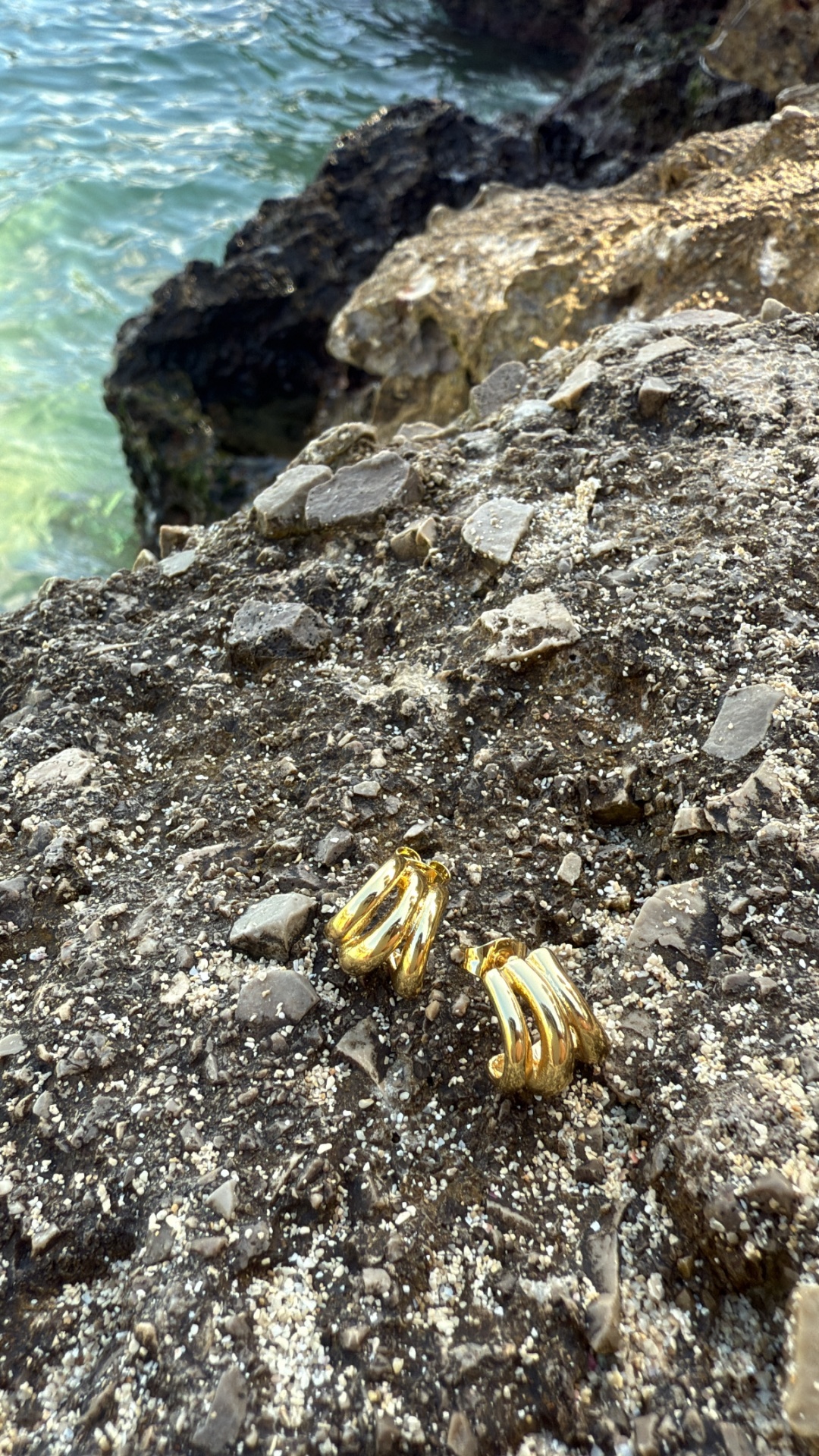 Brincos dourados curvos sobre rochas cinza perto do mar
