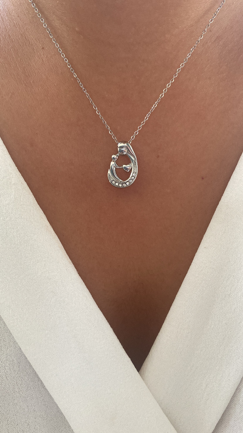 Colar prateado com pendente em forma de gancho, usado com blusa branca