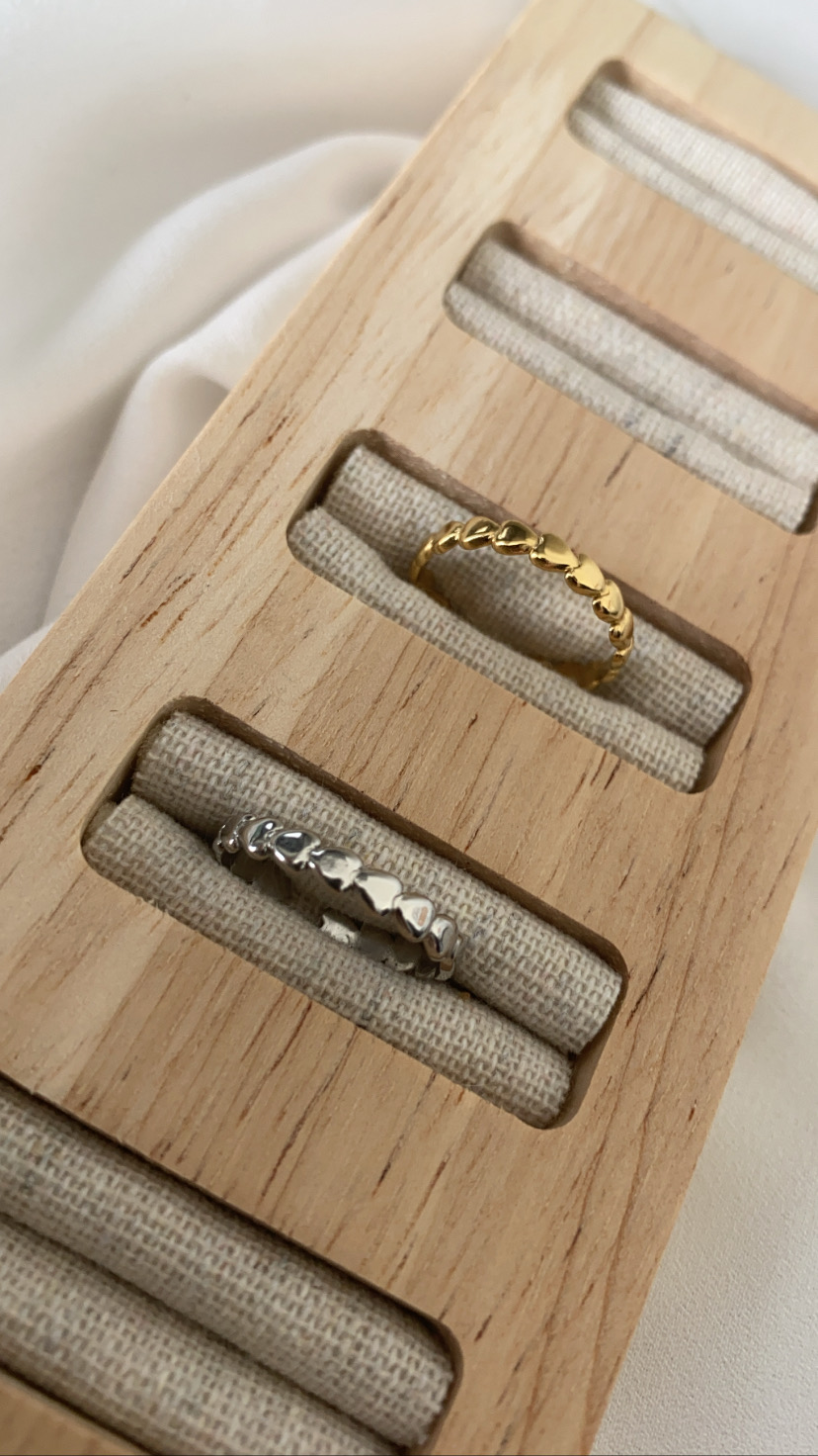 Anéis dourado e prateado com padrão de coração em mostruário de madeira clara com tecido bege