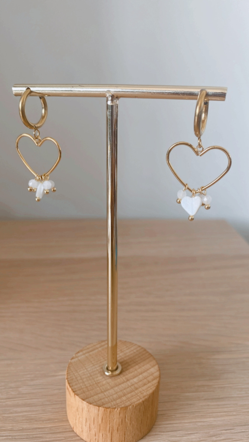Brincos dourados em forma de coração com pérolas em suporte de madeira