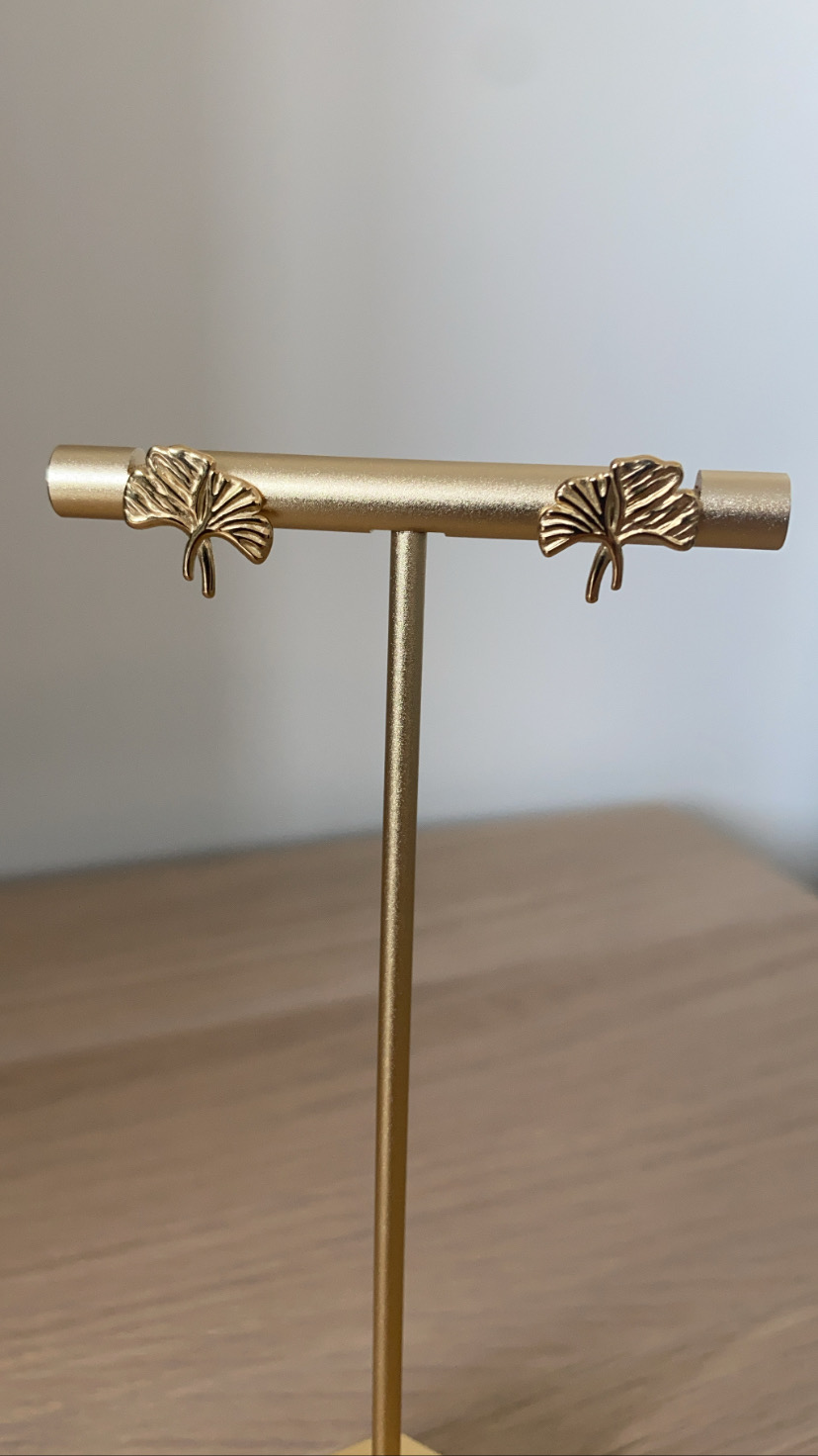 Brincos em metal dourado com formato de folha exibidos num suporte dourado