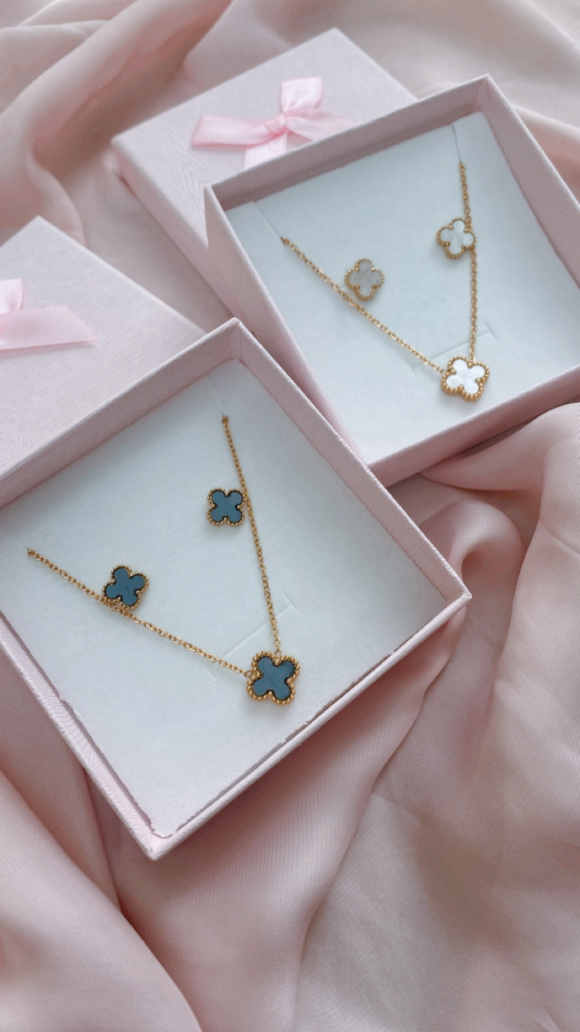 Conjunto de joalharia com colar e brincos em forma de flor azul e branco em caixas com laço cor-de-rosa