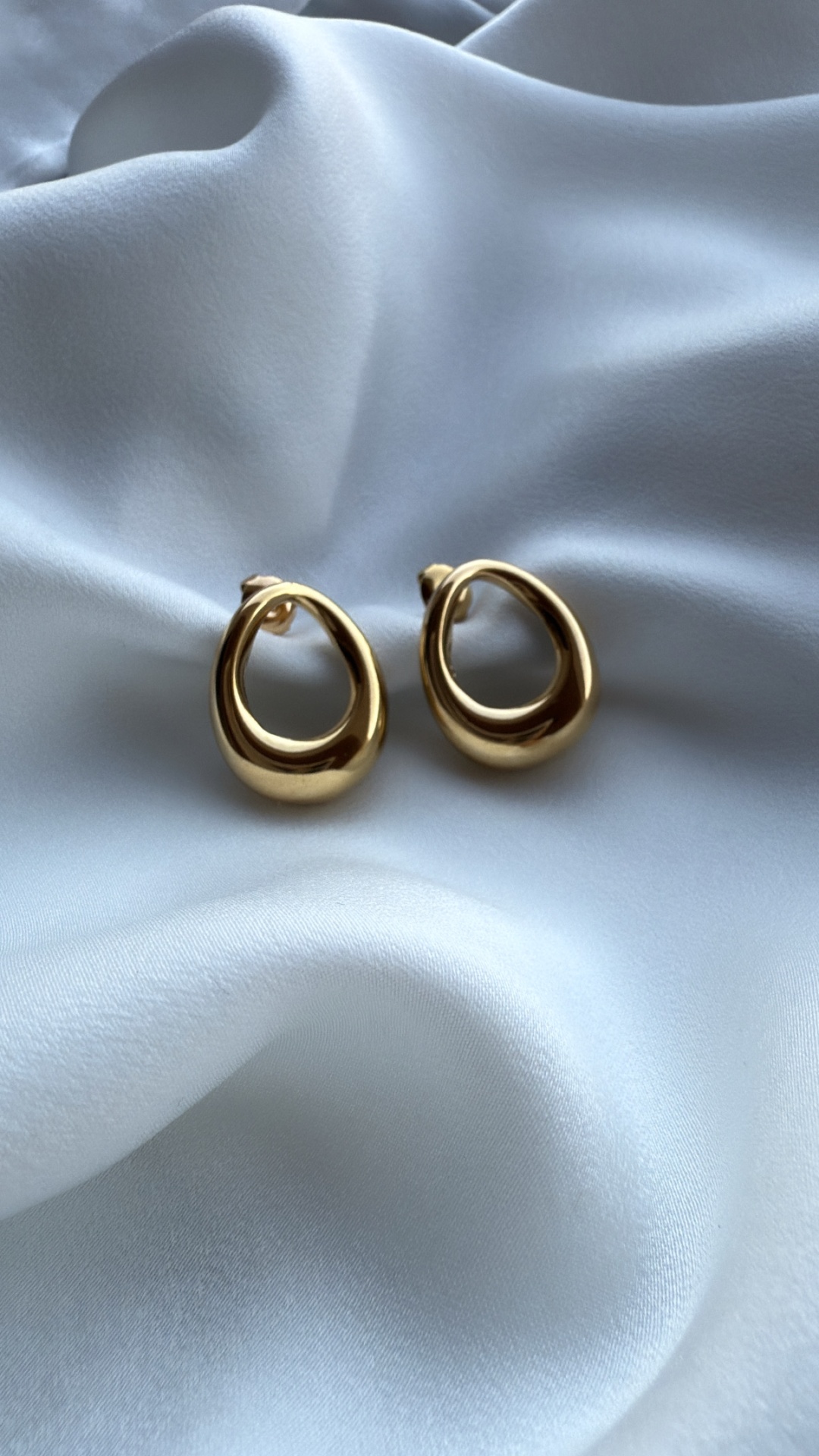 Brincos dourados ovais sobre tecido branco