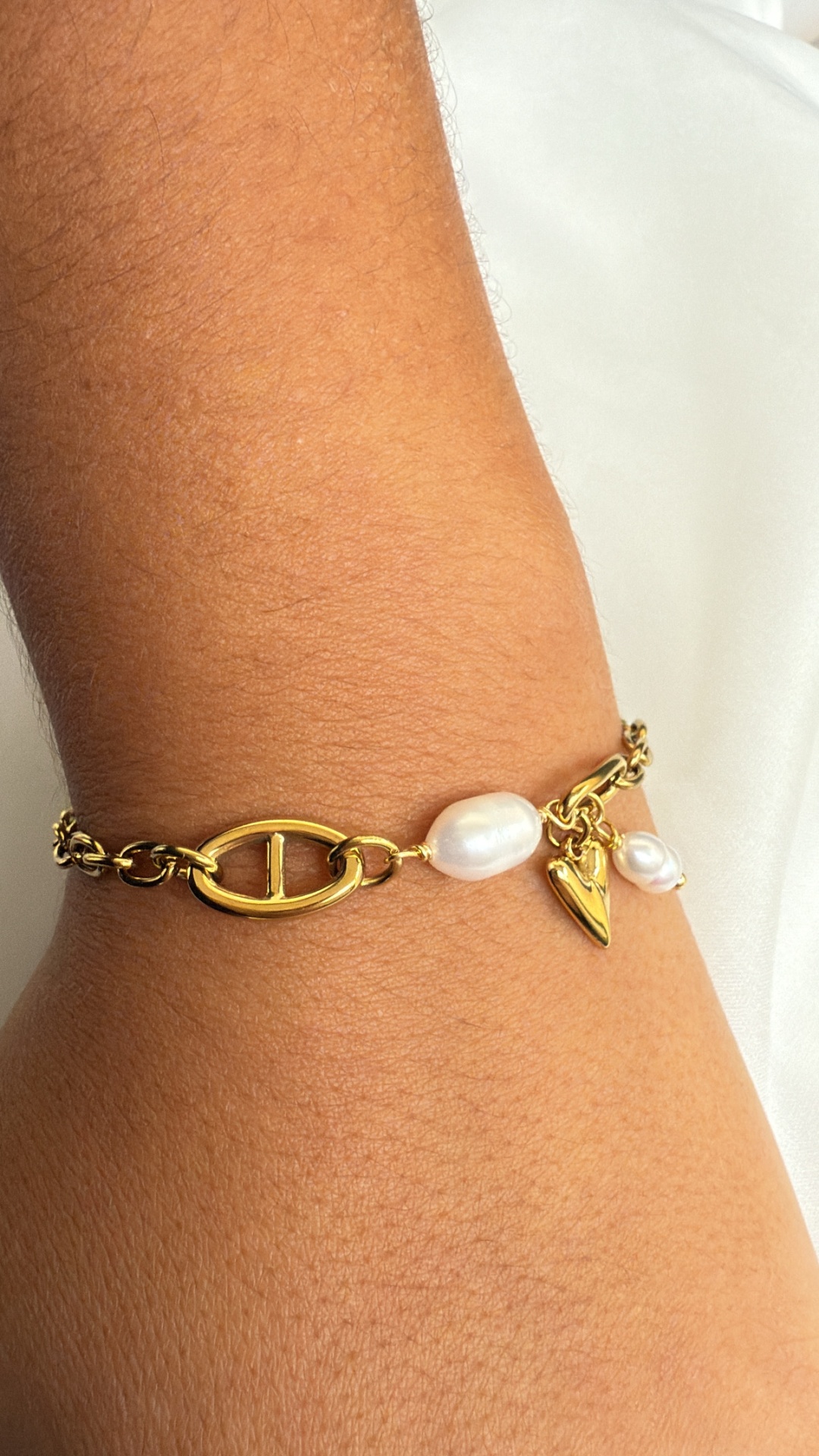 Pulseira dourada com pérolas e pendente de coração num pulso