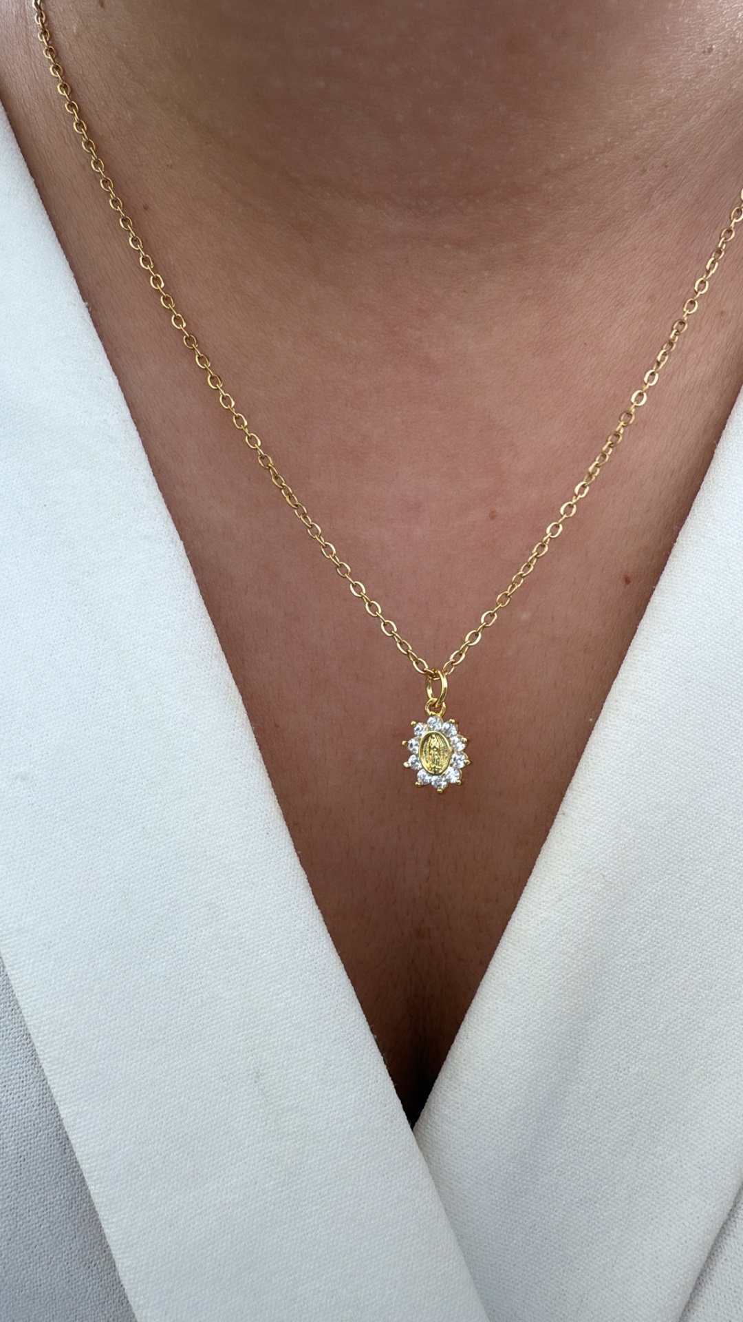 Colar dourado com pendente oval decorado, usado sobre pele e roupa branca