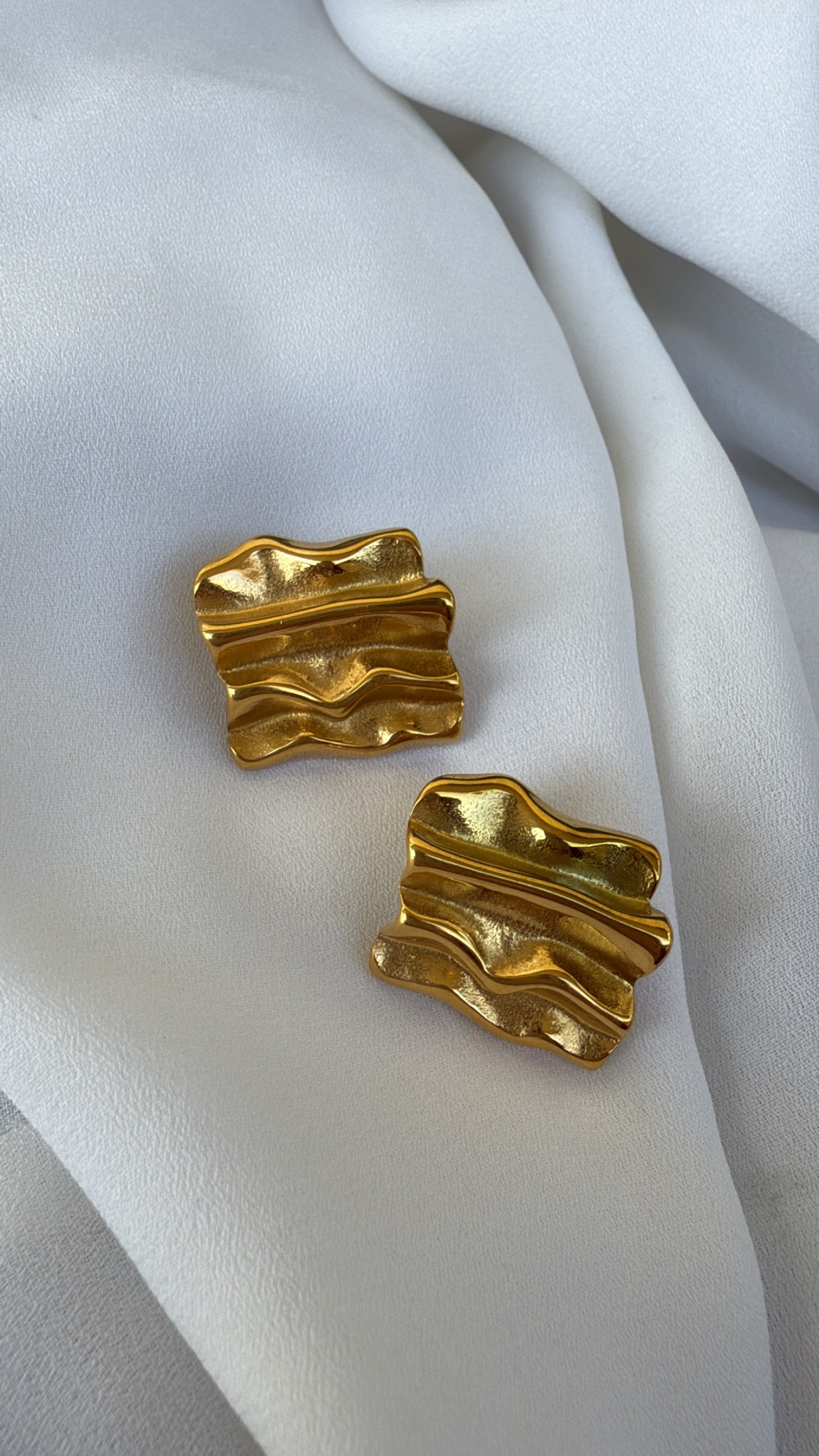 Par de brincos dourados ondulados sobre tecido branco