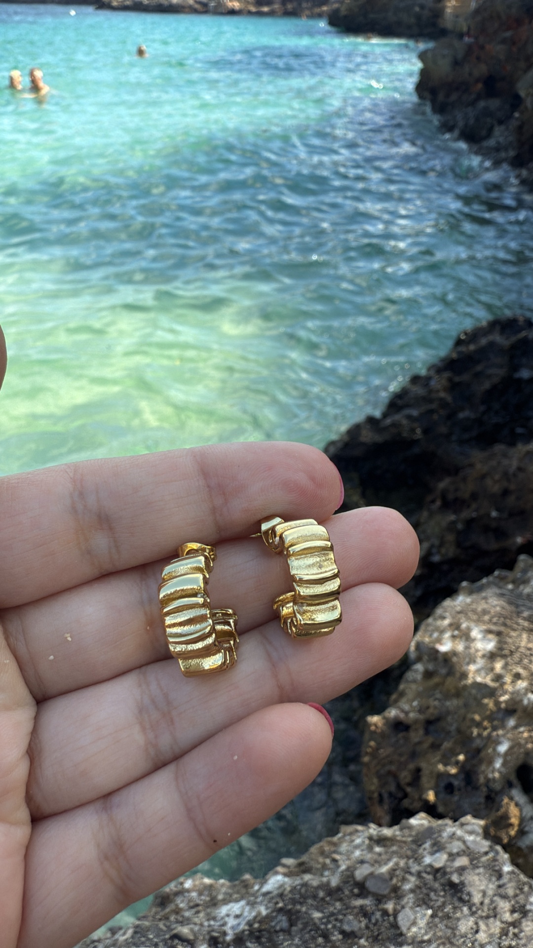 Brincos dourados em relevo segurados à frente do mar e rochas
