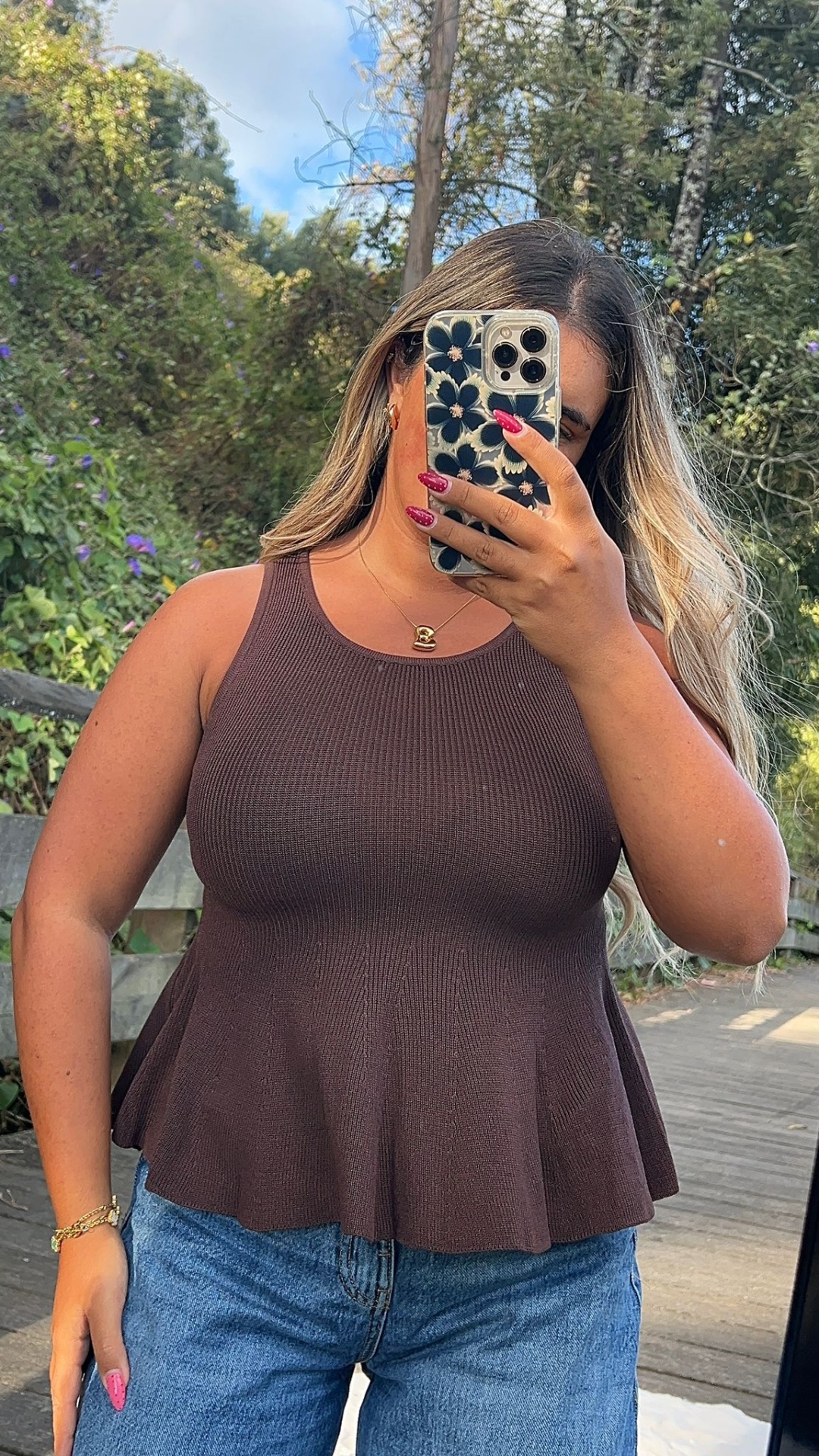 Top feminino de malha castanha com gola redonda e corte evasê, usado com calças de ganga azuis, selfie ao ar livre.