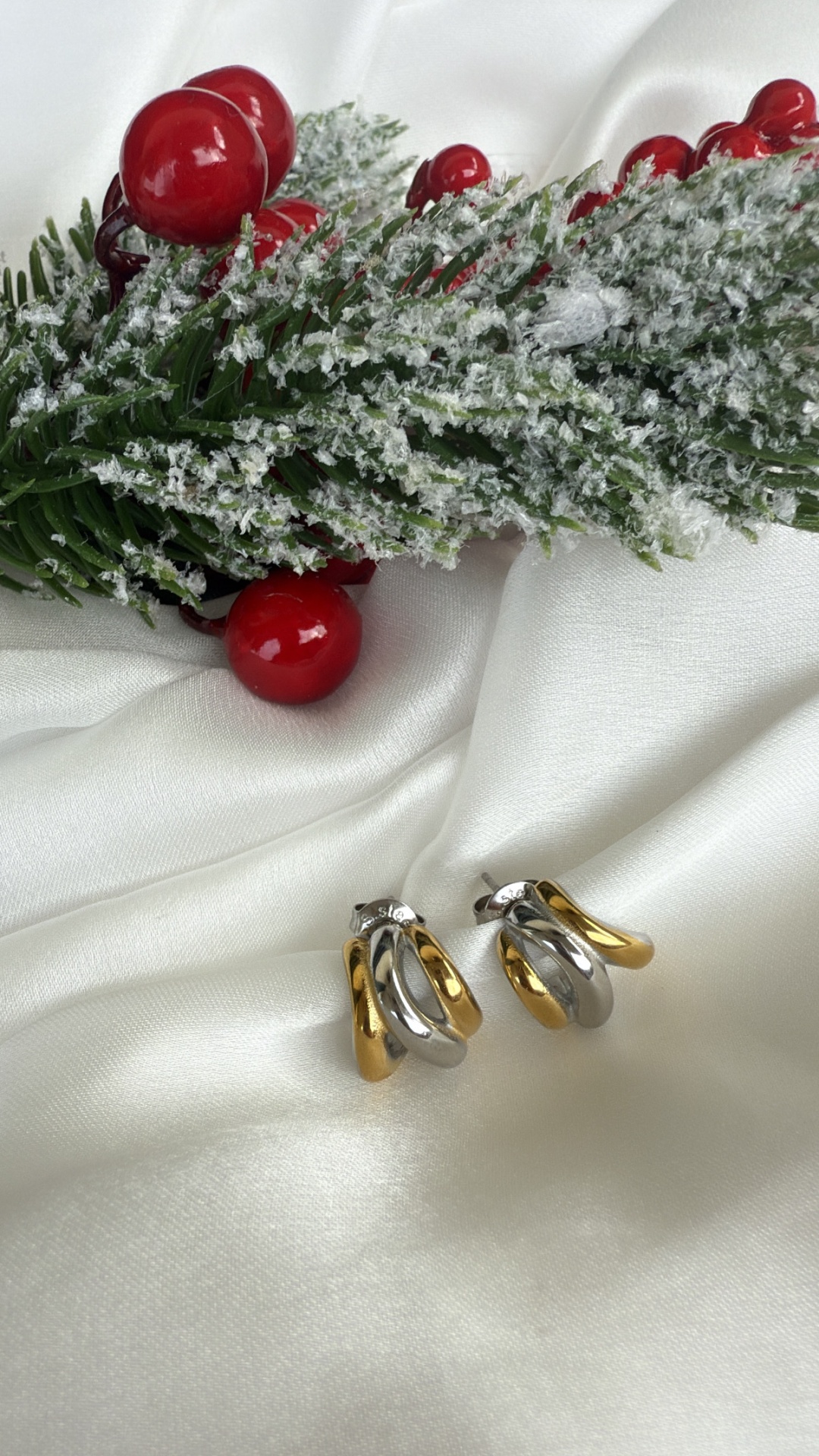 Brincos bicolor dourado e prateado sobre tecido branco com decoração festiva