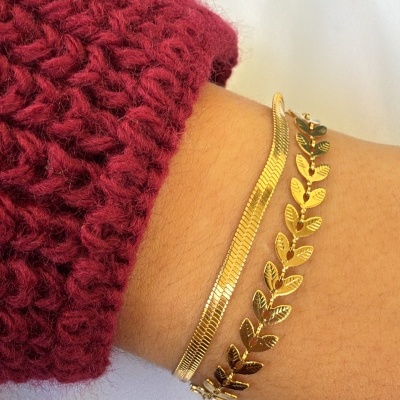 Duas pulseiras douradas com padrões distintos num pulso com manga vinho em malha grossa.
