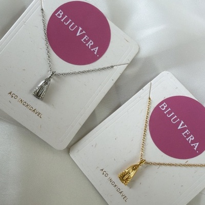 Colares BIJUVERA prateado e dourado em cartas brancas com círculo rosa sobre tecido branco