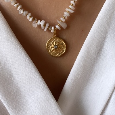 Colar com contas brancas e pendente dourado redondo sobre camisa branca