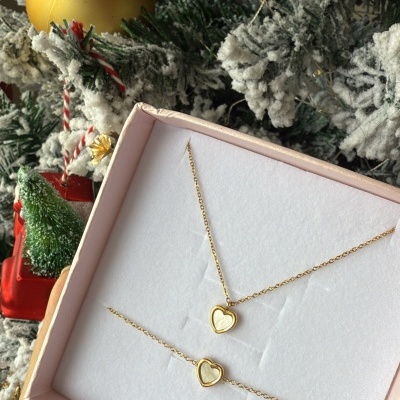 Conjunto de joias douradas com coração numa caixa rosa sobre fundo de árvore de Natal decorada.