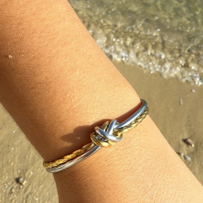 Pulseira de nó dourada e prateada no pulso junto à praia