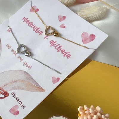 Pulseiras dourada e prateada com corações em cartão sobre tecido branco e caixa dourada com etiqueta Feliz Páscoa