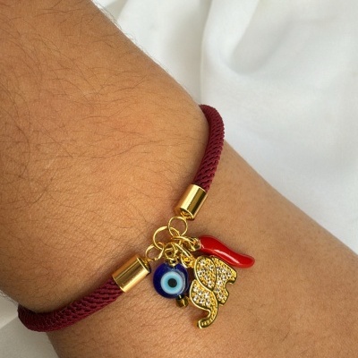Pulseira vermelha com pendentes dourados, olho azul e corno vermelho no pulso