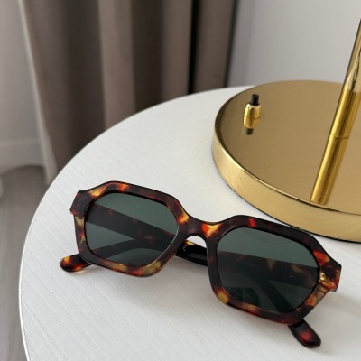 Óculos de sol com armação tartaruga e lentes escuras sobre mesa branca ao lado de candeeiro dourado