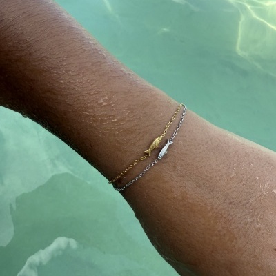 Pulseira dupla dourada e prateada com pássaros no pulso junto a água verde clara