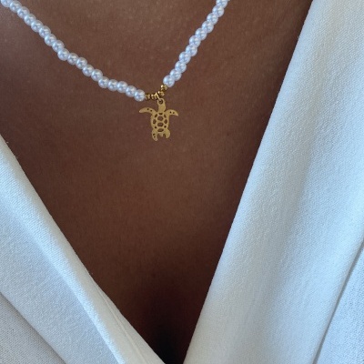 Colar de pérolas com pendente de tartaruga dourado sobre pele e roupa branca