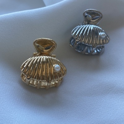acessórios em forma de concha dourado e prateado com pérola sobre tecido branco