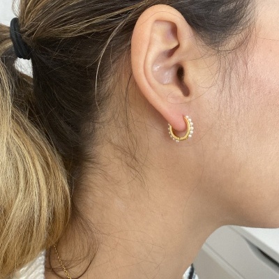 Brinco de argola dourada com pérolas numa orelha