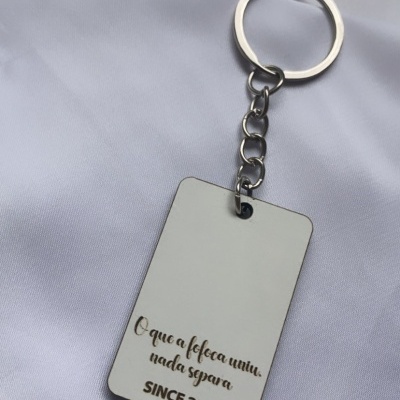 Porta-chaves retangular prateado com texto gravado, sobre tecido branco