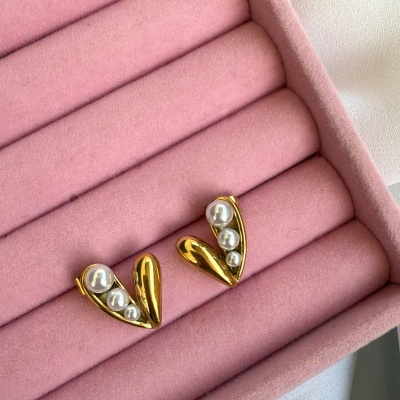 Brincos dourados em forma de coração com pérolas numa caixa rosa de veludo