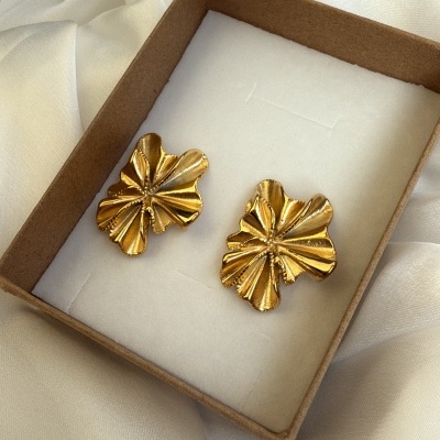 Brincos dourados em forma de folhas numa caixa de cartão sobre tecido de cetim branco