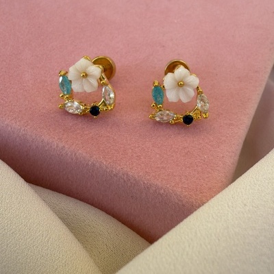 Brincos dourados com flores brancas e pedras coloridas sobre tecido rosa e bege