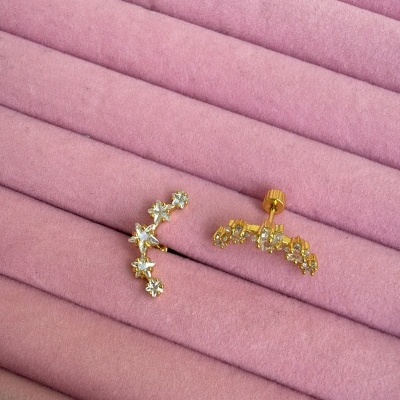 Brincos dourados com pedras em superfície almofadada rosa