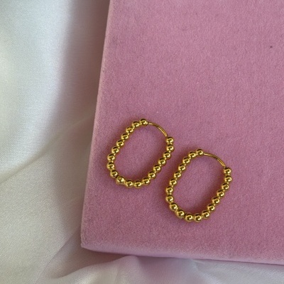 Brincos de argola dourados com contas sobre superfície rosa aveludada e tecido branco