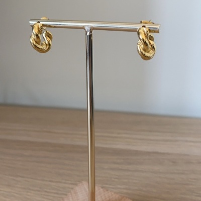 Brincos dourados entrelaçados em suporte metálico prateado com base de madeira