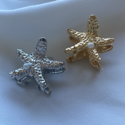 clips de cabelo em forma de estrela-do-mar prateado e dourado com pérola no centro sobre tecido branco