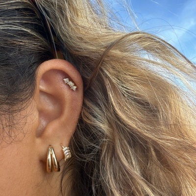 Orelha com três brincos dourados e cabelo em fundo de céu azul