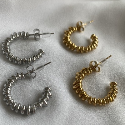 Dois pares de brincos argola, prateado e dourado, textura espiral metálica sobre tecido branco