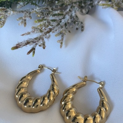 Brincos de argola dourada com textura ondulada sobre tecido branco com decoração de ramos verdes e bagas vermelhas