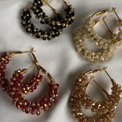 Quatro pares de brincos argola dourados com contas coloridas sobre tecido branco