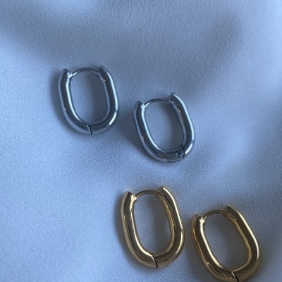 Dois pares de brincos argola oval em metal prateado e dourado sobre tecido branco