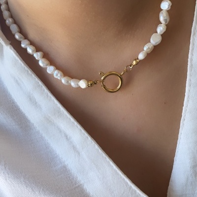 Colar de pérolas com fecho dourado sobre blusa branca