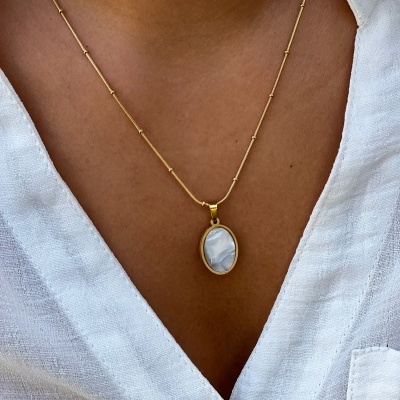 Colar dourado com pendente oval azul claro sobre camisa branca