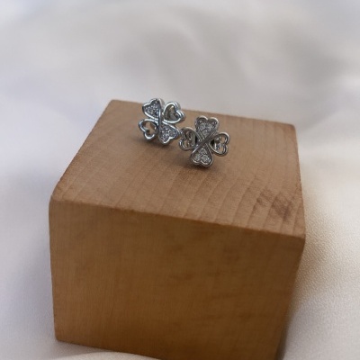 Brincos prateados em forma de trevo com pedras, sobre cubo de madeira