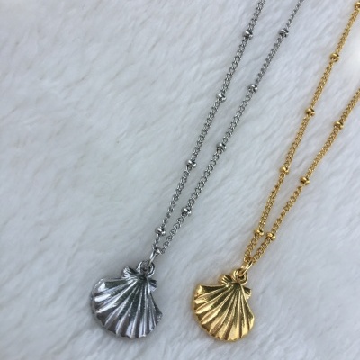 Colares com pendentes de concha em prata e dourado sobre superfície branca felpuda