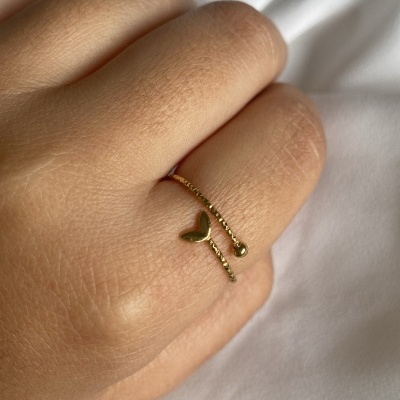 Anel dourado com coração e esfera numa mão sobre tecido branco