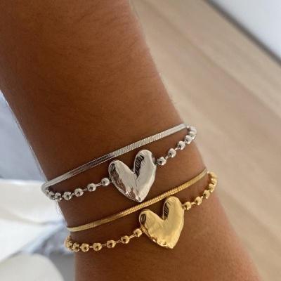 Pulseiras dourada e prateada com corações metálicos no pulso