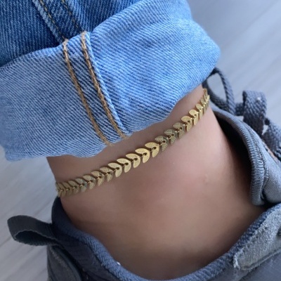 Pulseira de tornozelo dourada com design de folhas usada com calças de ganga e sapatos de desporto cinzentos